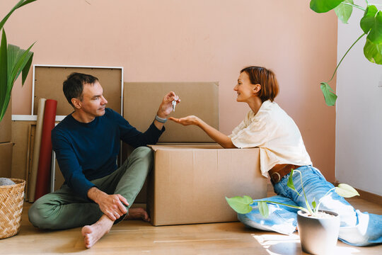 A mature caucasian man cheerfully shows house keys to his smiling wife among unpacked moving boxes. Joyful home buying and successful mortgage approval concept.