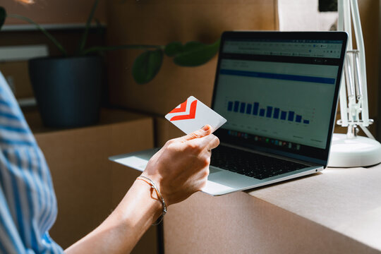 A person holds a credit card while analyzing financial charts on a laptop screen near moving boxes. Online banking and digital mortgage payment concept.