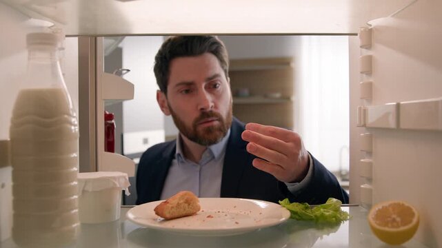 Confused Caucasian business man opening fridge with empty shelves eating crumbs male employer businessman finding one egg bottle of water eat snack dieting kitchen lifestyle POV inside refrigerator