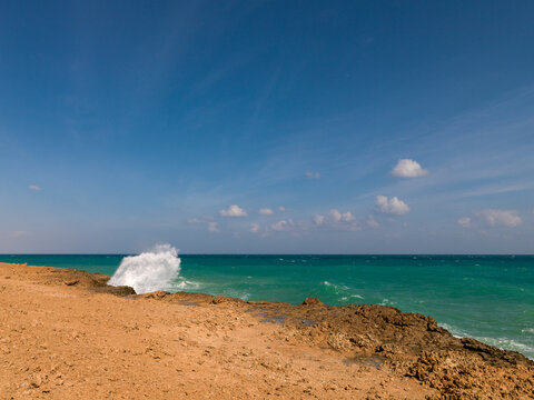 A wave crashes against a rocky shoreline under a clear sky, Obock Region, Khor angar, Djibouti