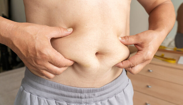 Male hands grasp roll of excess fat at waist, symbolizing excess weight, obesity, and need for weight loss or dieting. Healthy lifestyle, self-care, weight control