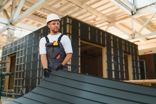 Worker installing siding on modular house in factory