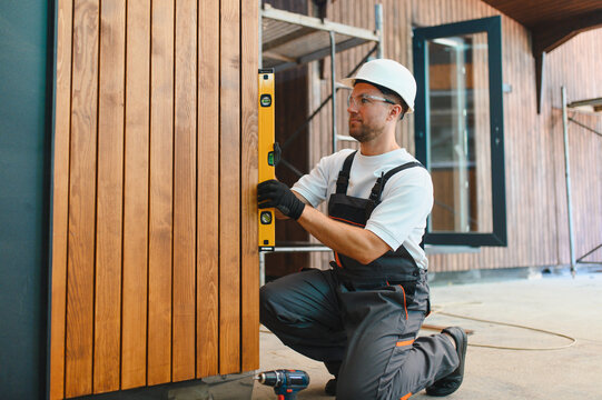 Worker checking level of modular house wood siding