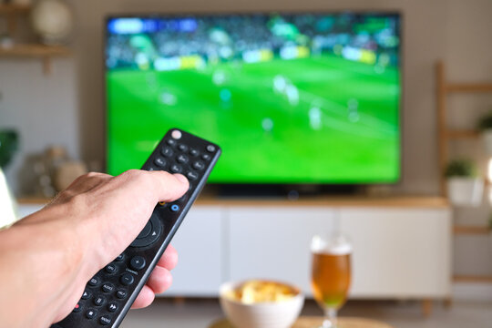 Hand holding remote control changing tv channel during soccer game