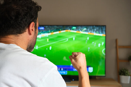 unrecognizable man watching a soccer match on television and celebrating a goal.