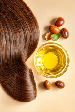 Long brown hair next to a bowl of amber-colored hair oil and argan fruits on a white background creates a simple, clean look for health and beauty