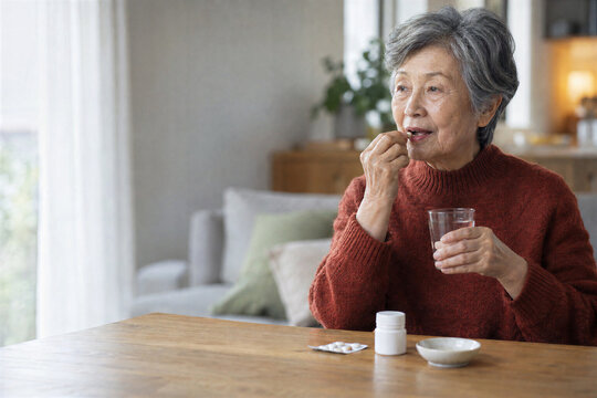 Asian senior woman taking daily vitamins with water at home