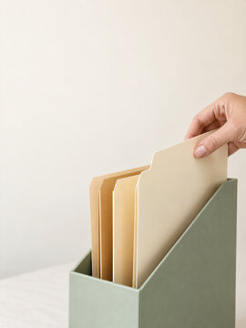 Hand files a folder into an office organizer. Folders line a muted green holder, leaving generous copy space. Filing represents organization, planning, and productive time management.