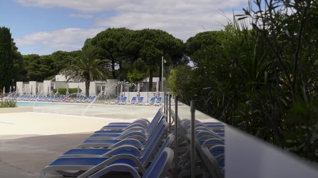 Rows of blue sun loungers beside a landscaped vacation club pool under tall trees