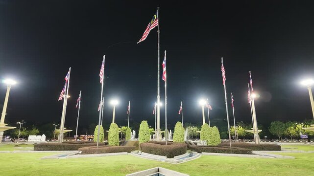 Slow motion shot of Malaysian national flags (Jalur Gemilang) fluttering on tall flagpoles under night illumination at Dataran Putra in Putrajaya, Malaysia.