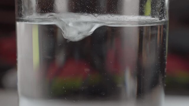 Air bubbles suspended in clear water inside a transparent glass create delicate details near the surface. The background remains softly blurred to emphasize the water.