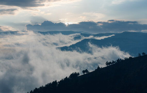 Dramatic mountain landscape with low clouds and mist rolling over the forested hills at sunset