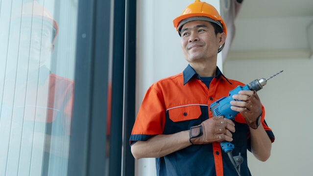 Professional construction worker holding a power drill while wearing a safety helmet and uniform