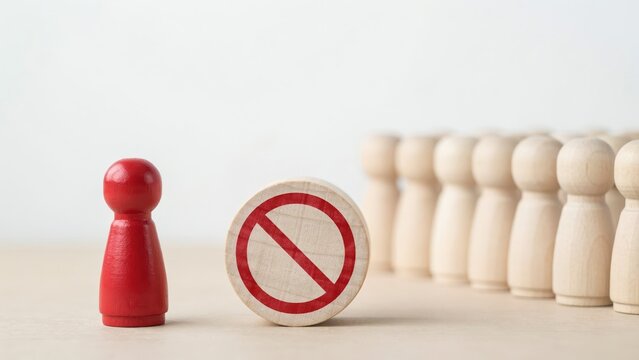 Red wooden peg figure separated from a group by a forbidden symbol for discrimination or exclusion concept