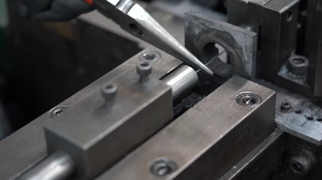 Cutting tool machining a polished steel cylinder clamped in a lathe fixture inside a small metal parts workshop