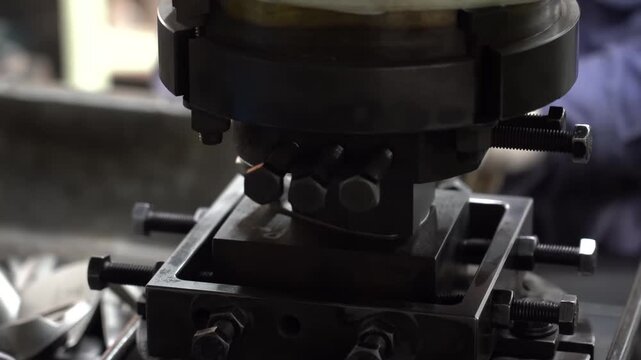 Gloved worker feeds a forged golf club head into a trimming press between heavy steel die blocks