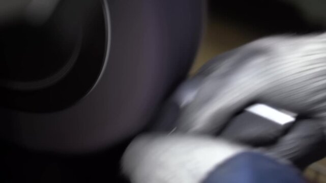 Craftsman polishes a chrome golf iron head against a spinning buffing wheel with both gloved hands