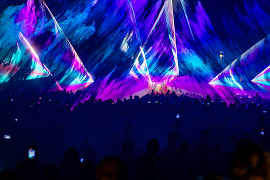 Vibrant blue and purple laser light show projected over crowd 