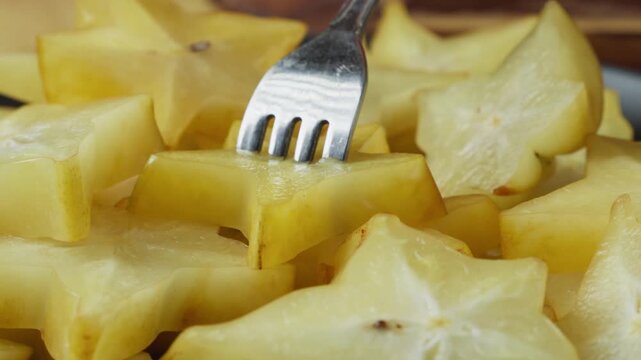 Person using a fork to pick up a pile of freshly sliced star fruit