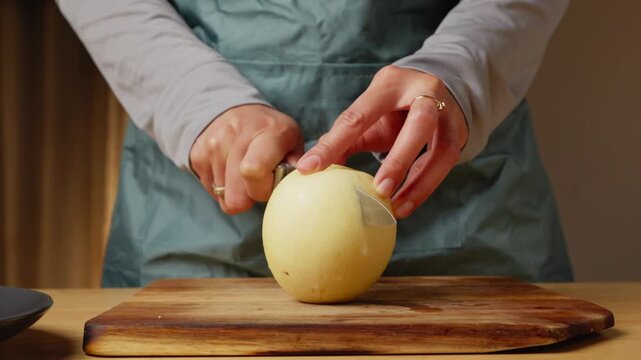 Person cutting a fresh pear in half with a kitchen knife on a wooden cutting board