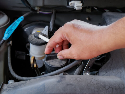 a mechanic's hand holding a cigarette while working on an open car engine in a garage. Suitable for editorial articles, workplace safety campaigns, health risk presentations, and automotive service to