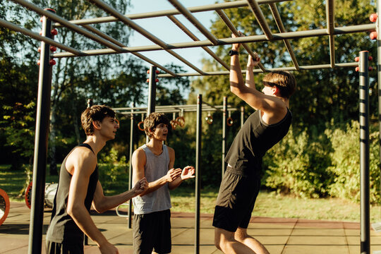Team of young guys working out together on summer gymnastic rings outdoors.