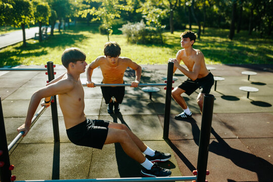 Shirtless Gen Z Adolescent Athletes Practicing Outdoor Calisthenics in Summer Park.