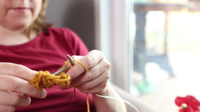 Close-up of hands knitting with yellow yarn for slow living and digital detox