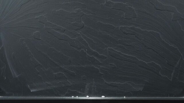 Small White Particles Falling And Settling On A Dark Textured Slate Board