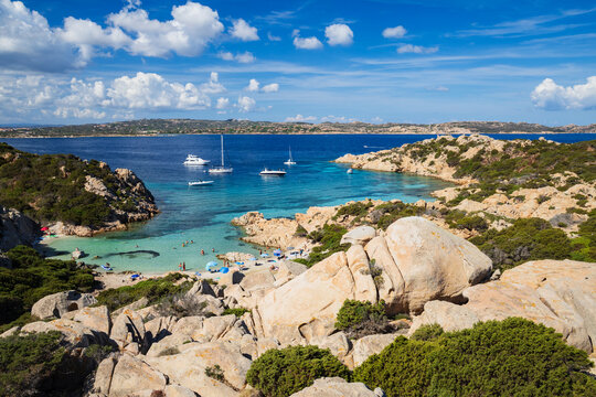 Capsized cove with boats and swimmers on the rocky coast of caprera