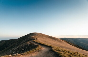 Obraz premium 青空の下、なだらかな山頂へ曲がりくねって続く稜線の登山道