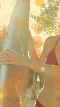Vertical video: Model grasping board smiling as cam pulling back with orange bokeh over for fashion