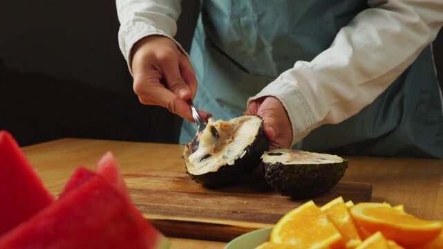 Person using a spoon to scoop the soft white flesh from a freshly cut soursop