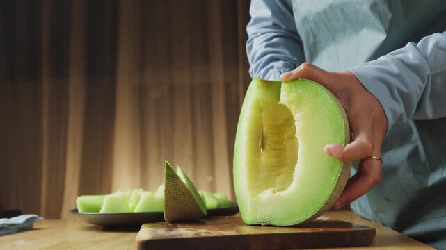 Cutting fresh honeydew melon into slices on a wooden cutting board