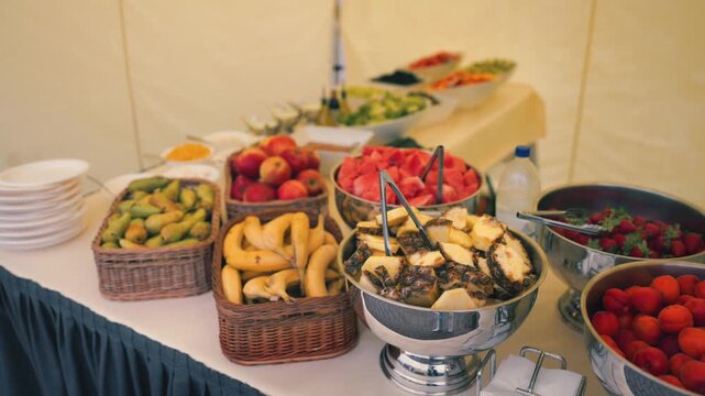 Colorful fruit buffet featuring assorted fruits like bananas, apples, and watermelon displayed in baskets and bowls under a tent at a festive outdoor gathering