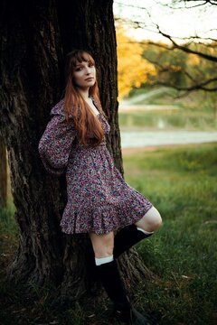 Woman leans against a tree by the lake during sunset in a natural setting