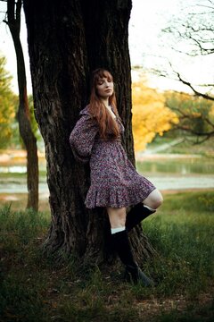 Woman leans against a tree by the lake during sunset in a natural setting