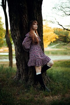 Woman leans against a tree by the lake during sunset in a natural setting
