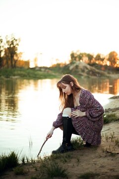 Young woman interacts with water at riverbank during sunset
