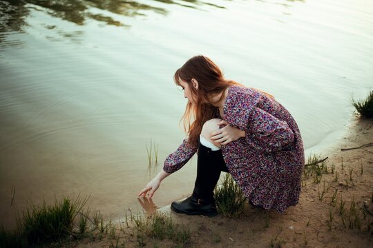 Young woman interacts with water at riverbank during sunset