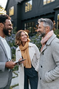 Friendly real estate consultation with agent and two clients outside a modern home by landscaped garden for brochure and listing