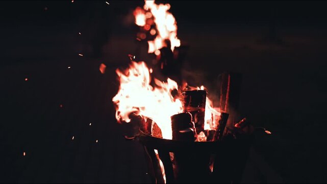 Bright flames dance in metal fire pits filled with logs, illuminating the night as sparks fly, creating a warm atmosphere in a cozy outdoor setting