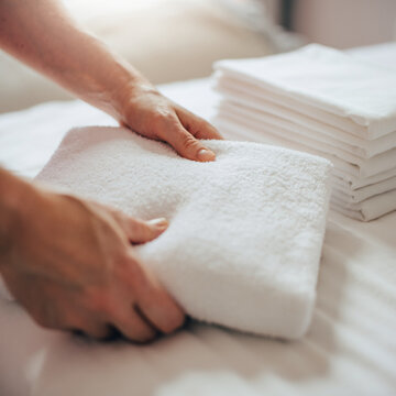 Hands folding clean towel on bed with laundry stack