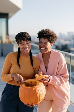 Mother and adult daughter scooping pumpkin seeds for halloween and autumn greeting card on a sunny rooftop scene