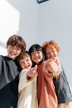 Smiling diverse group of children close together pointing at camera for kids background and school friendship scene with warm daylight