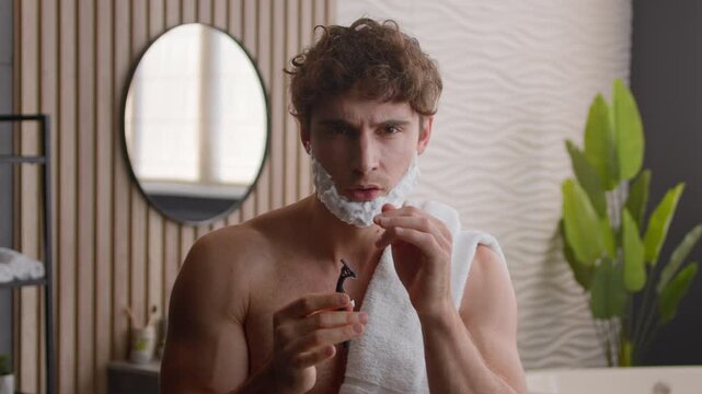 Joyful Caucasian millennial man guy singing and dancing in bathroom with shaving foam on beard happy funny male enjoying morning grooming routine holding razor listening to music playful facial care