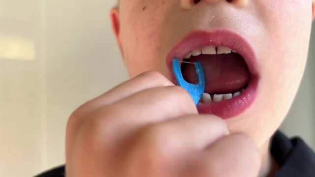 Child with primary teeth cleans between teeth with a floss pick, showing visible enamel changes. Dental hygiene, oral care, pediatric dentistry.