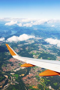Aerial commercial aircraft passenger window seat point of view on take off. Airplane wing above towns farmland and mountains seen through aircraft window during flight travel transportation tourism