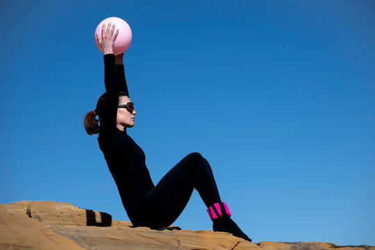 Woman in Black Sportswear with Pilates Ball on Rocks