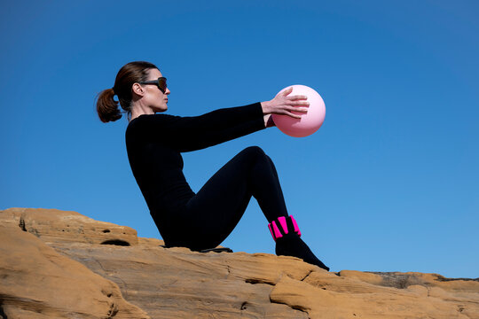 Woman Practicing Pilates on a Rocky Shore with sports ball